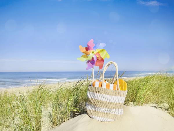 Ein gefüllte Strandtasche steht im Sand. Gesund im Sommer: Das gehört in die Reiseapotheke